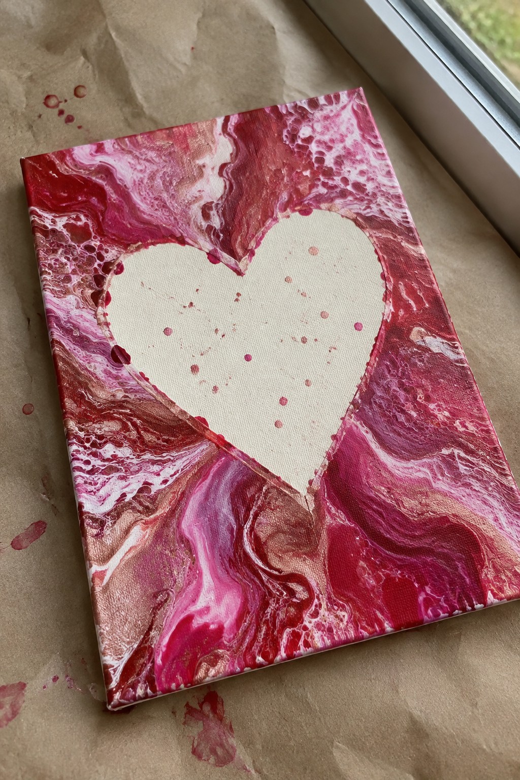 Canvas with white heart amid red pink marbled acrylic pour on brown paper