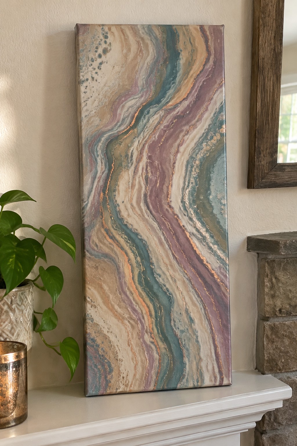 Abstract fluid art painting with teal purple gold swirls on white mantel beside plant