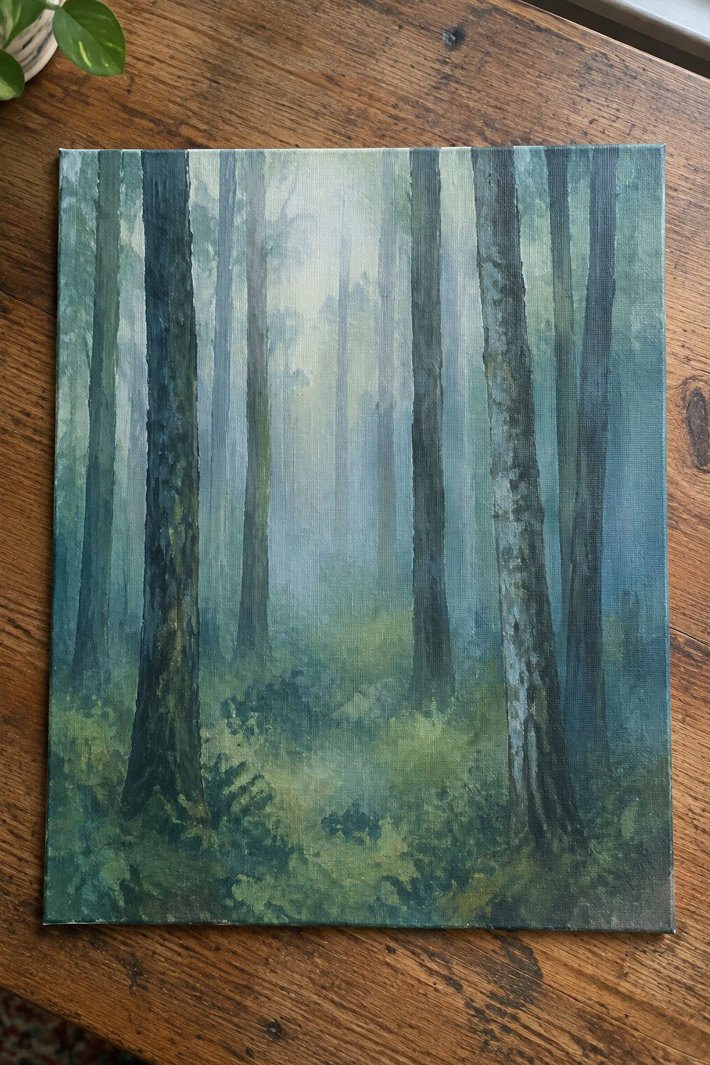 Misty forest painting with tall blue-green tree trunks on wooden table