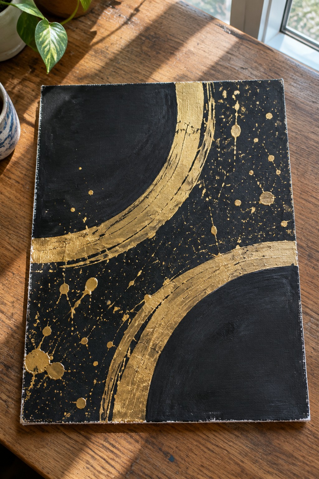 Abstract black and gold painting with curved strokes and splatters on wooden table