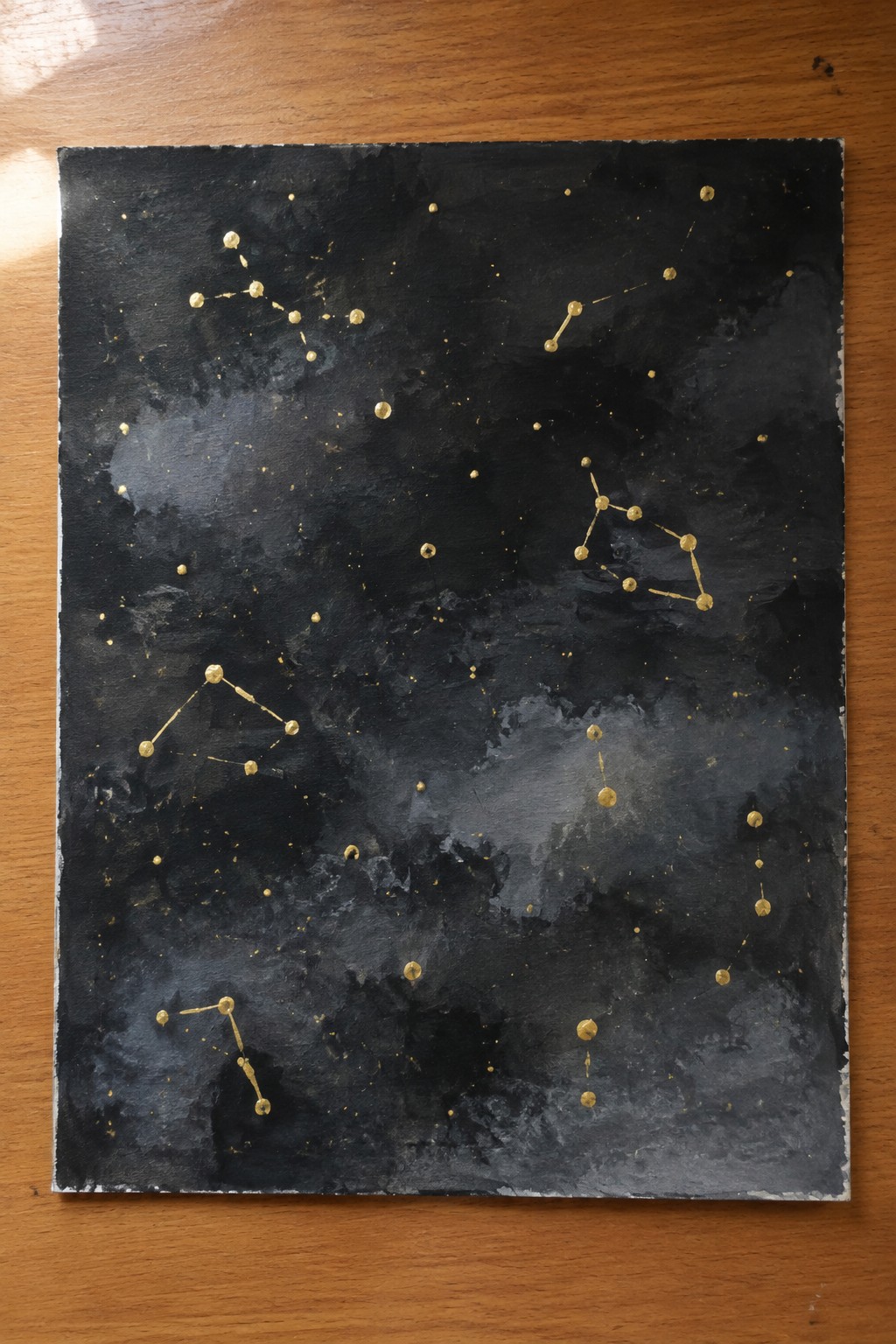Textured black painting with golden dots forming constellations and scattered specks