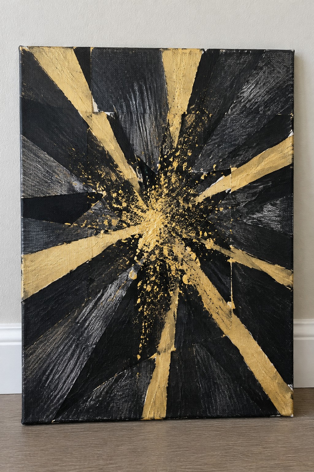 Abstract black and gold starburst painting with splatters on canvas against wall