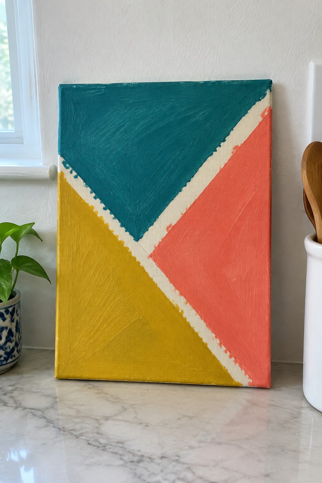 Abstract geometric painting with teal, yellow, coral sections and white lines on marble counter