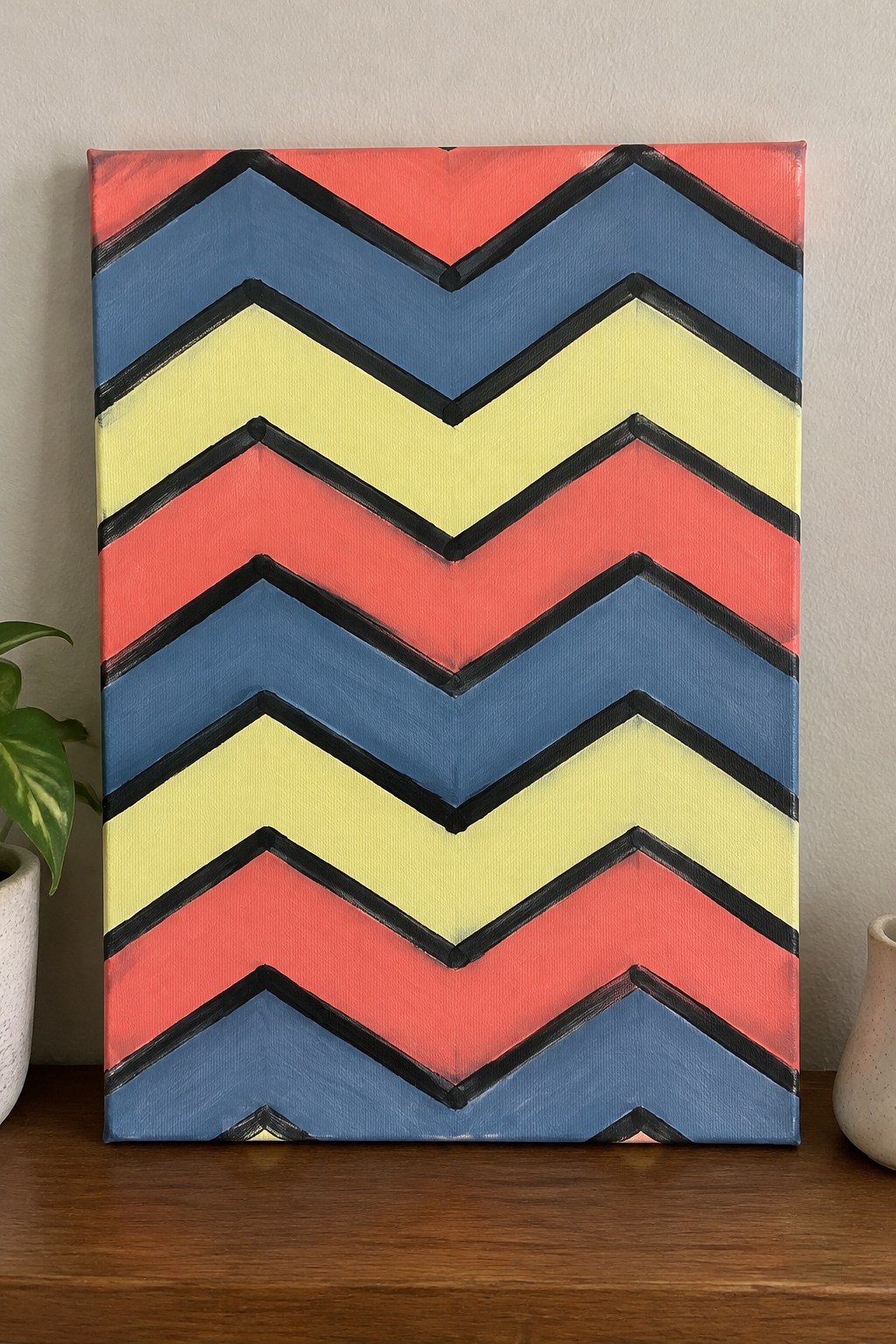 Colorful chevron canvas painting with red blue yellow stripes and black outlines on wooden shelf