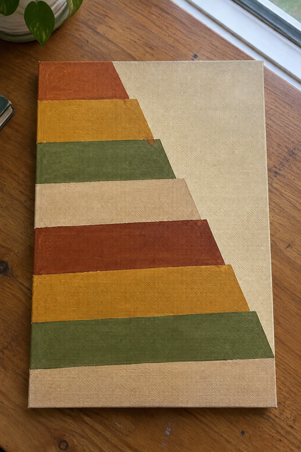 Abstract painting with diagonal stepped stripes in orange, yellow, green, brown, beige on wooden table