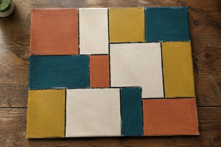 Abstract geometric canvas with orange, teal, yellow, white, and rust rectangular blocks on wood.