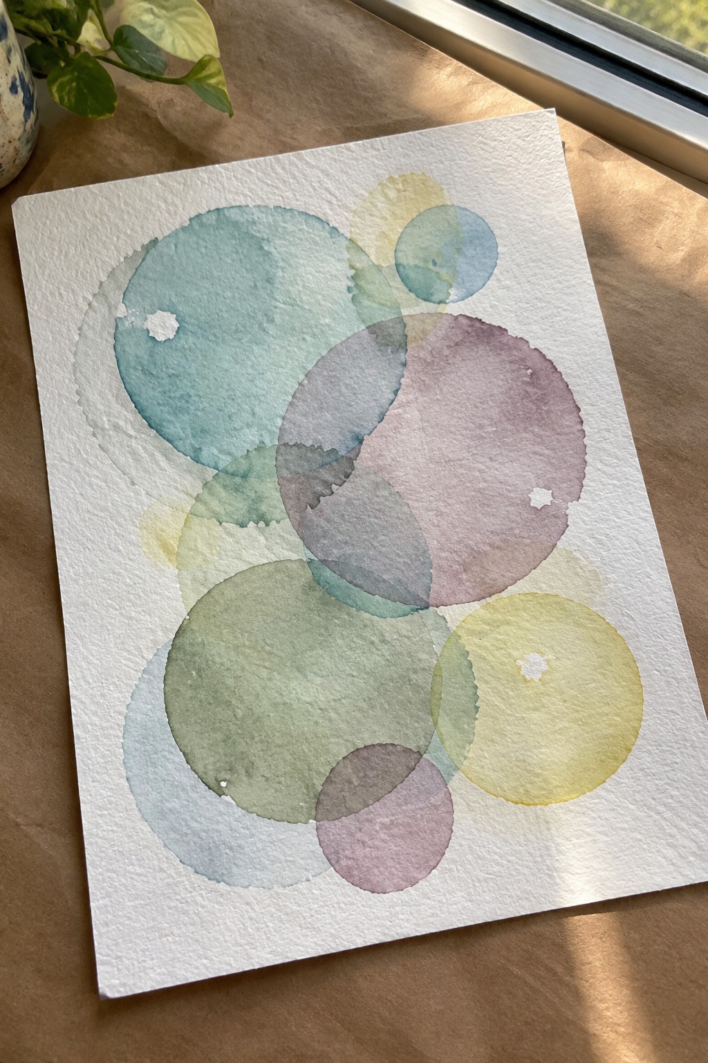 Watercolor painting of overlapping circles in teal, green, purple, and yellow on white paper.