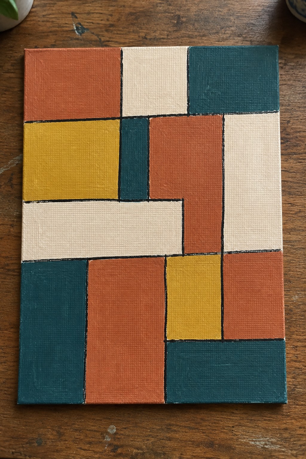 Abstract geometric canvas with orange, teal, yellow, white, and rust rectangular blocks on wood.