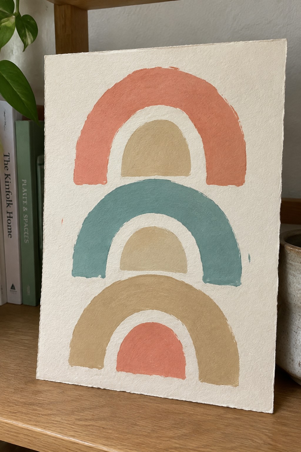 Abstract painting of three stacked arched rainbows in coral, teal, and brown on white paper