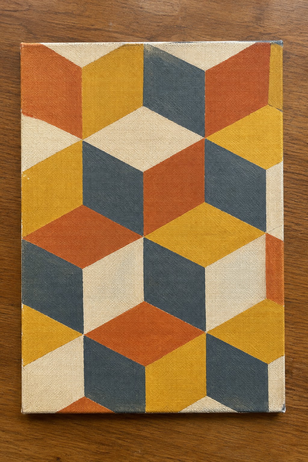 Geometric canvas painting with orange, yellow, blue, and cream interlocking shapes on wood