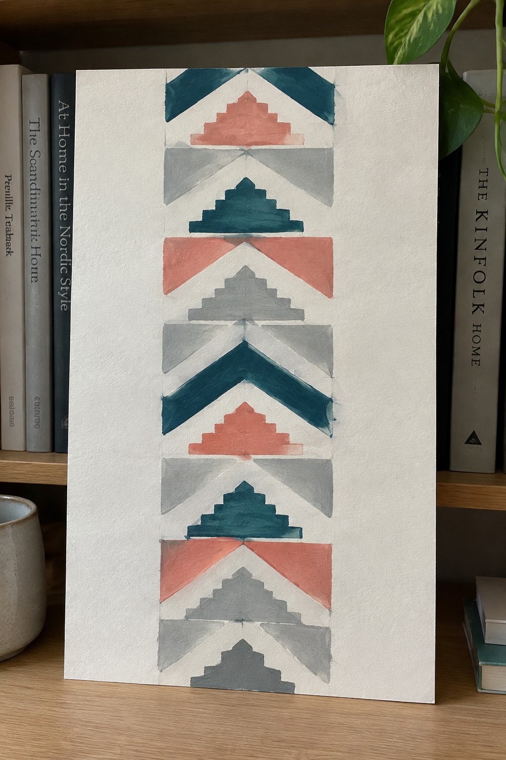 Geometric watercolor with teal coral gray triangles and chevrons on paper between books