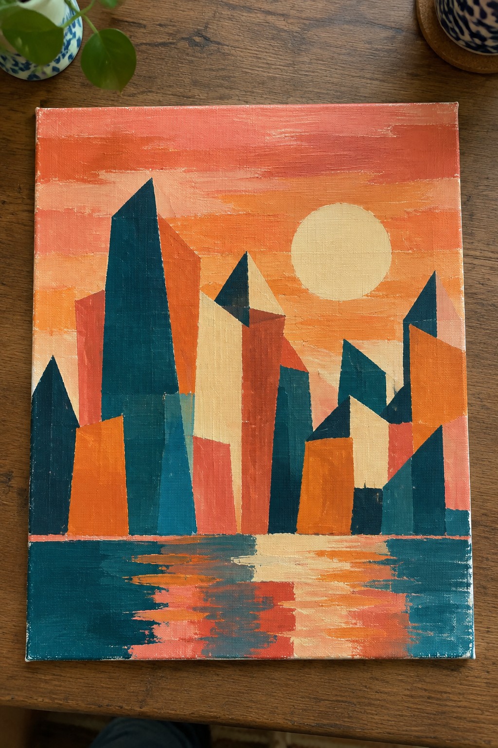 Abstract geometric cityscape with angular teal-orange buildings, pink sunset sky, and water reflections