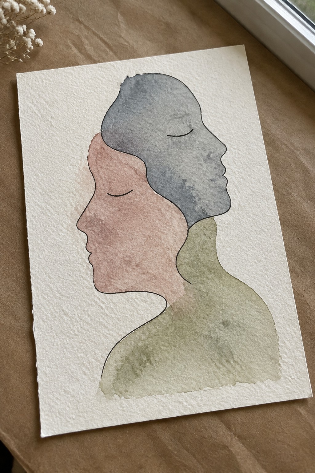 Two overlapping watercolor profile faces with closed eyes in pink, gray, and green.