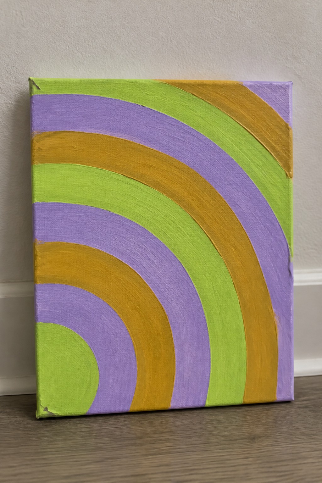 Abstract painting on canvas with curving lime green, purple, and gold stripes against wall.