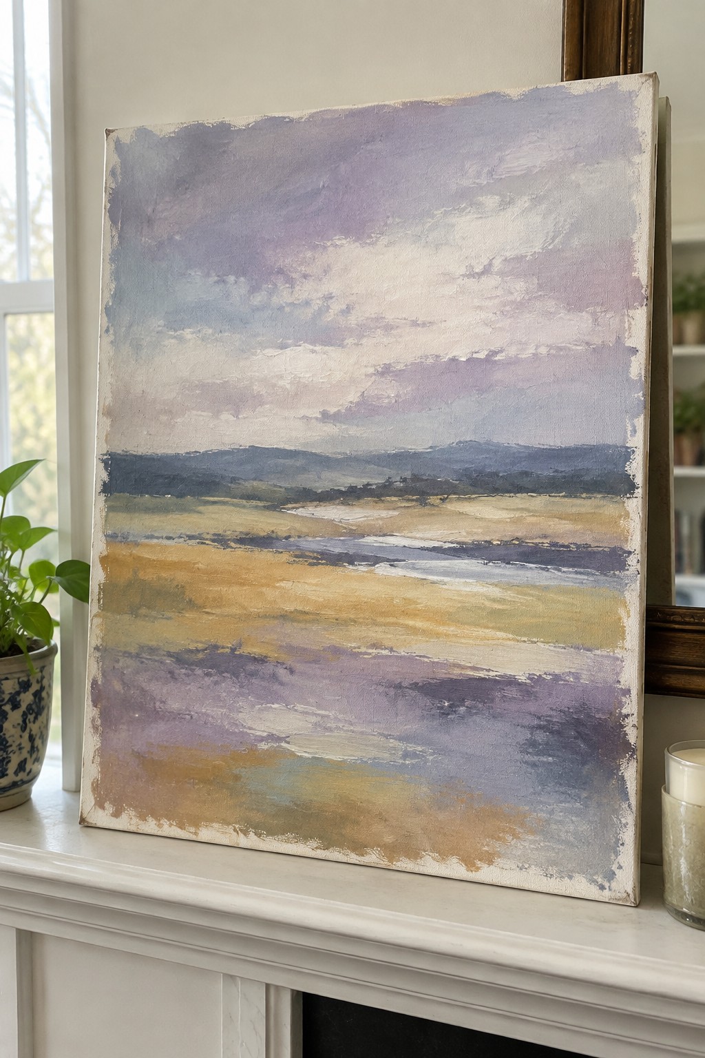 Abstract landscape painting in soft purples, blues, and golds on white mantel beside plant