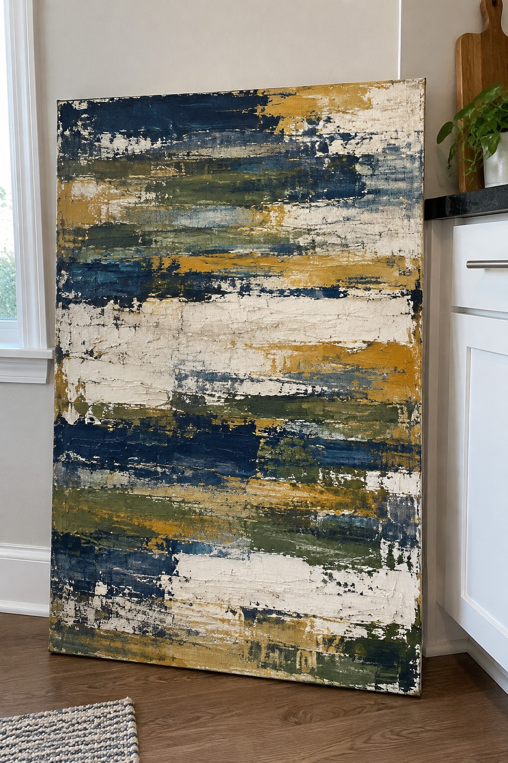 Abstract painting with blue, yellow, green brushstrokes leaning against kitchen wall