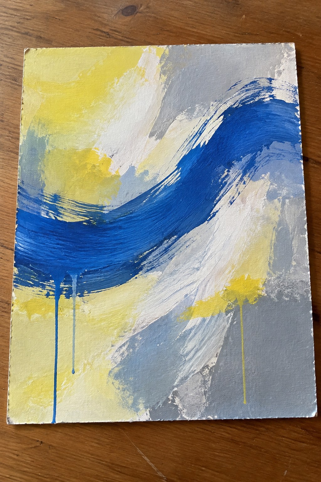 Abstract painting with bold blue brushstrokes, yellow accents, and drips on wood.