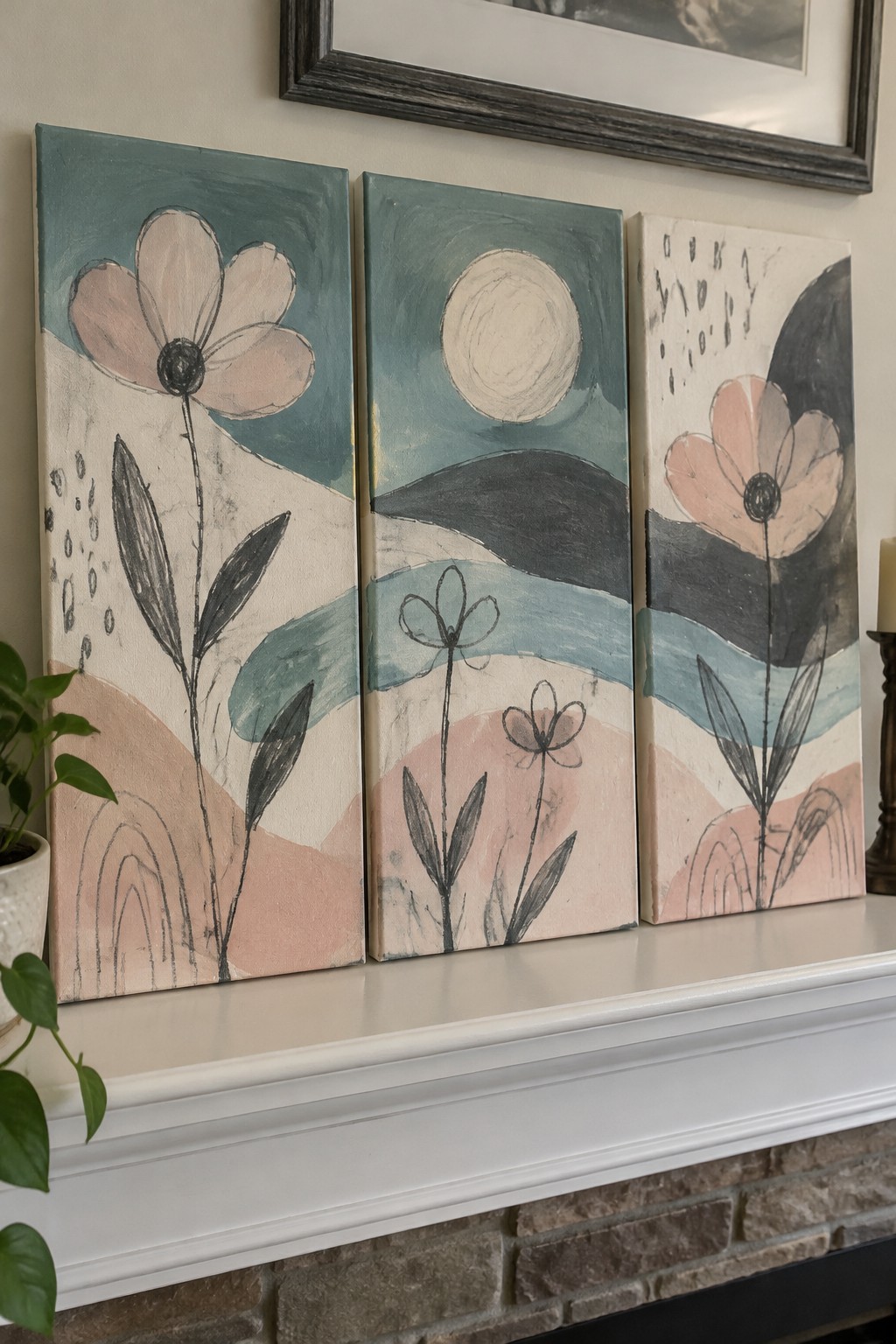Three abstract floral paintings in teal and pink on white mantel above fireplace