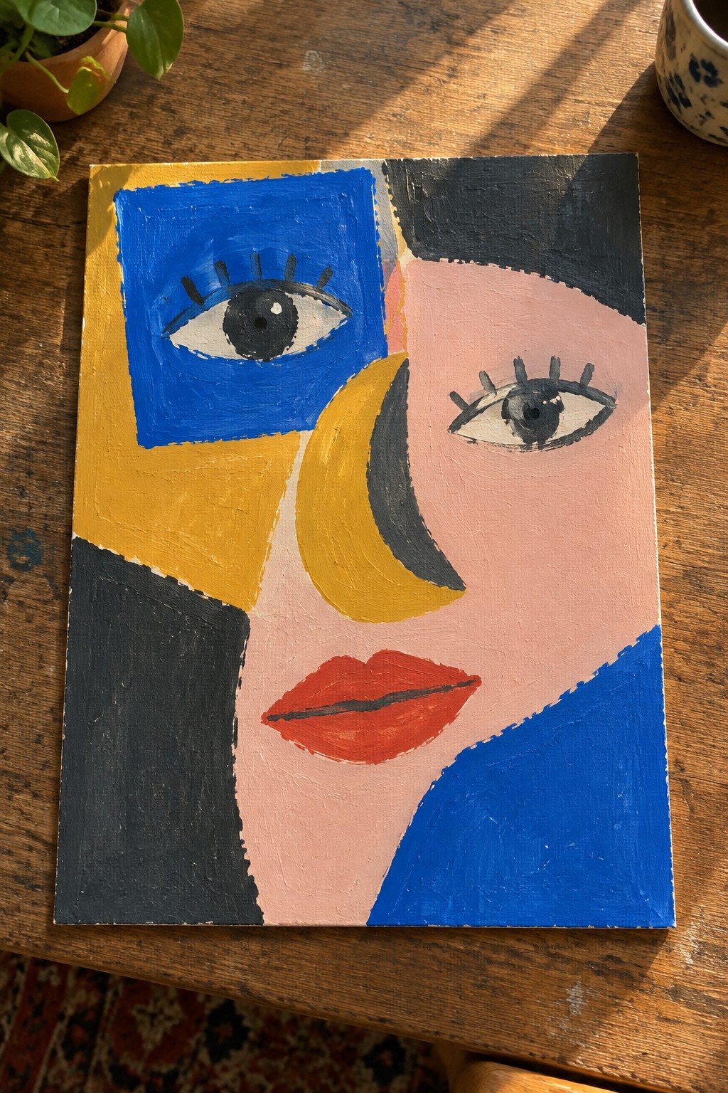 Abstract cubist painting of face with blue eye, yellow shapes, red lips on wood