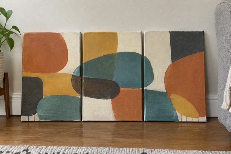 19 Coordinated Abstract Painting Triptychs for Modern Wall Displays Three abstract paintings with orange, teal, and yellow shapes on wooden floor beside plant