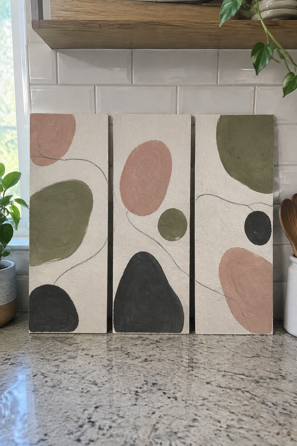 Three abstract panels with organic shapes in muted earth tones on kitchen counter