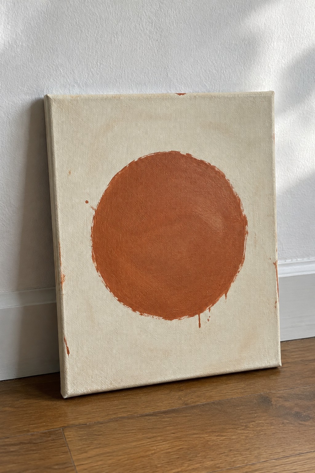 Leaning canvas with large dripping orange circle on off-white textured background