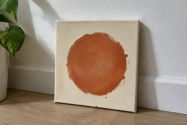 Leaning canvas with large dripping orange circle on off-white textured background