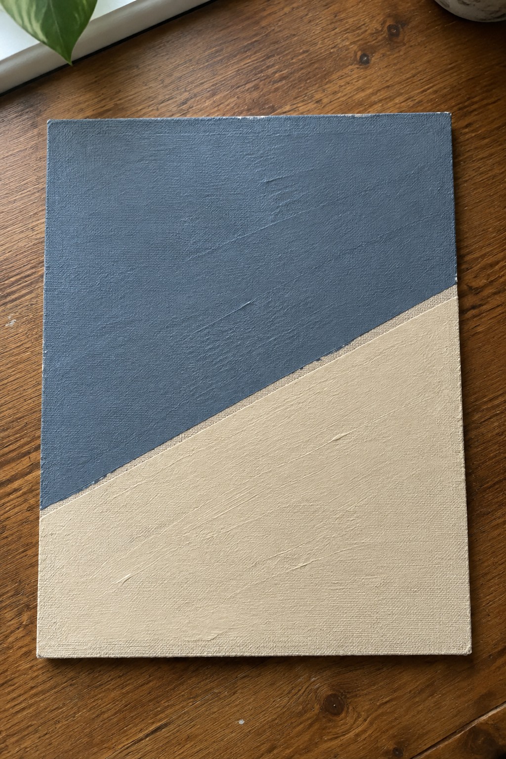 Abstract canvas with blue upper section and beige lower half on wooden table