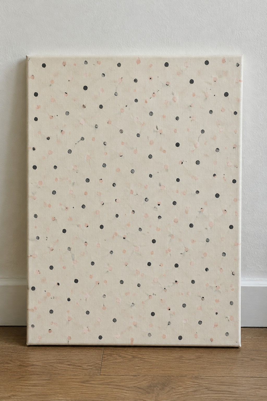Abstract canvas with scattered black and peach dots leaning against wall on wood floor