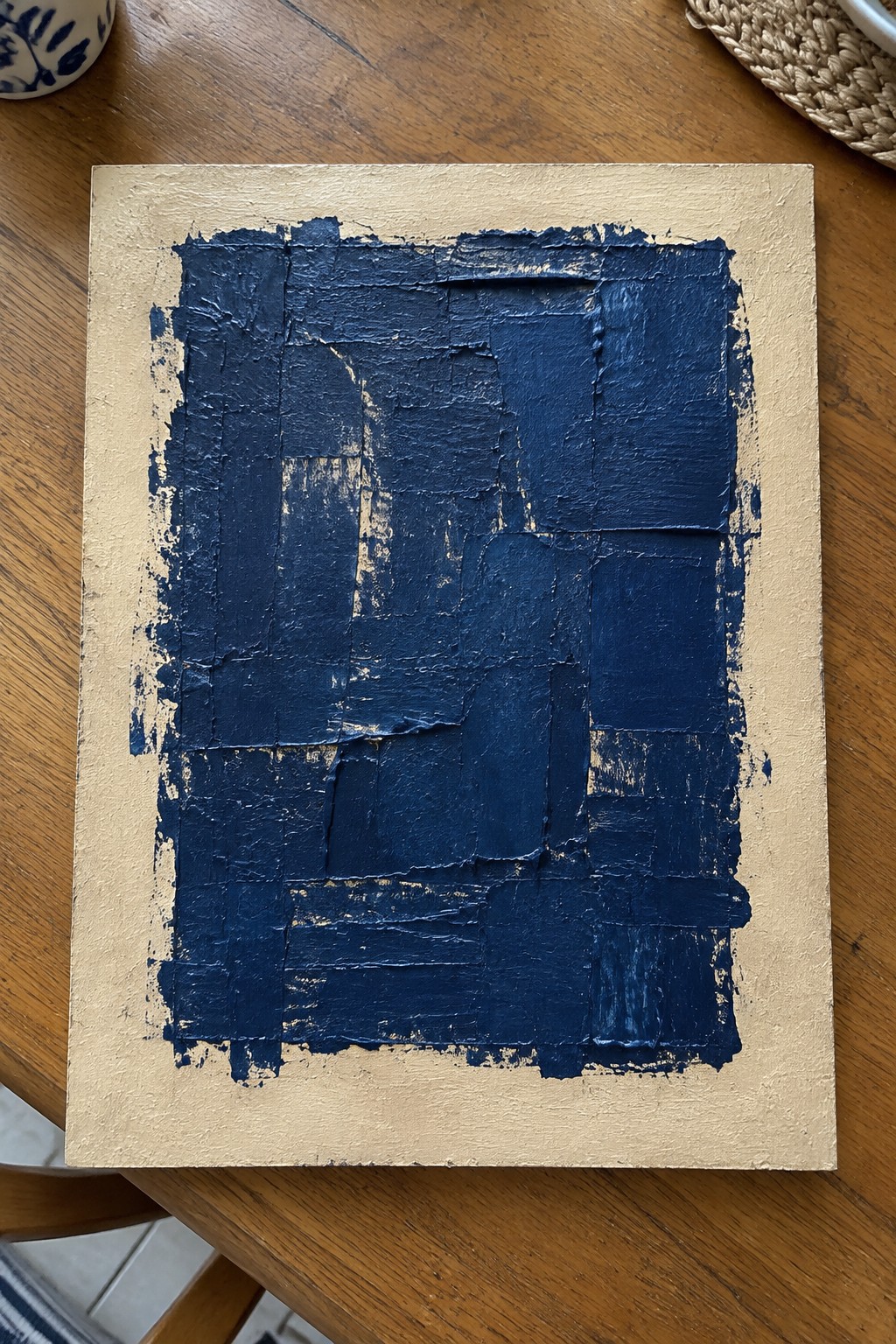Thick dark blue abstract painting with textured strokes on gold canvas on wood table.