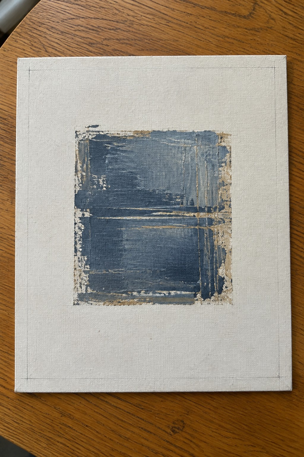 Abstract painting with dark blue brushstrokes and gold edges on white canvas
