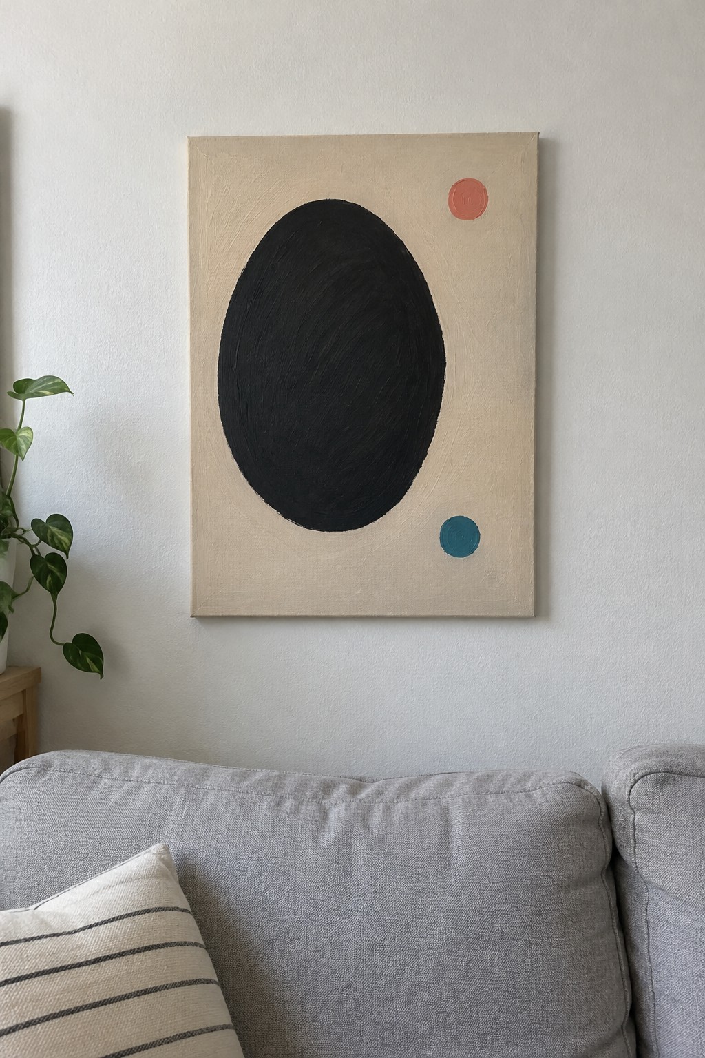 Abstract painting with black oval, red and teal dots above gray couch.