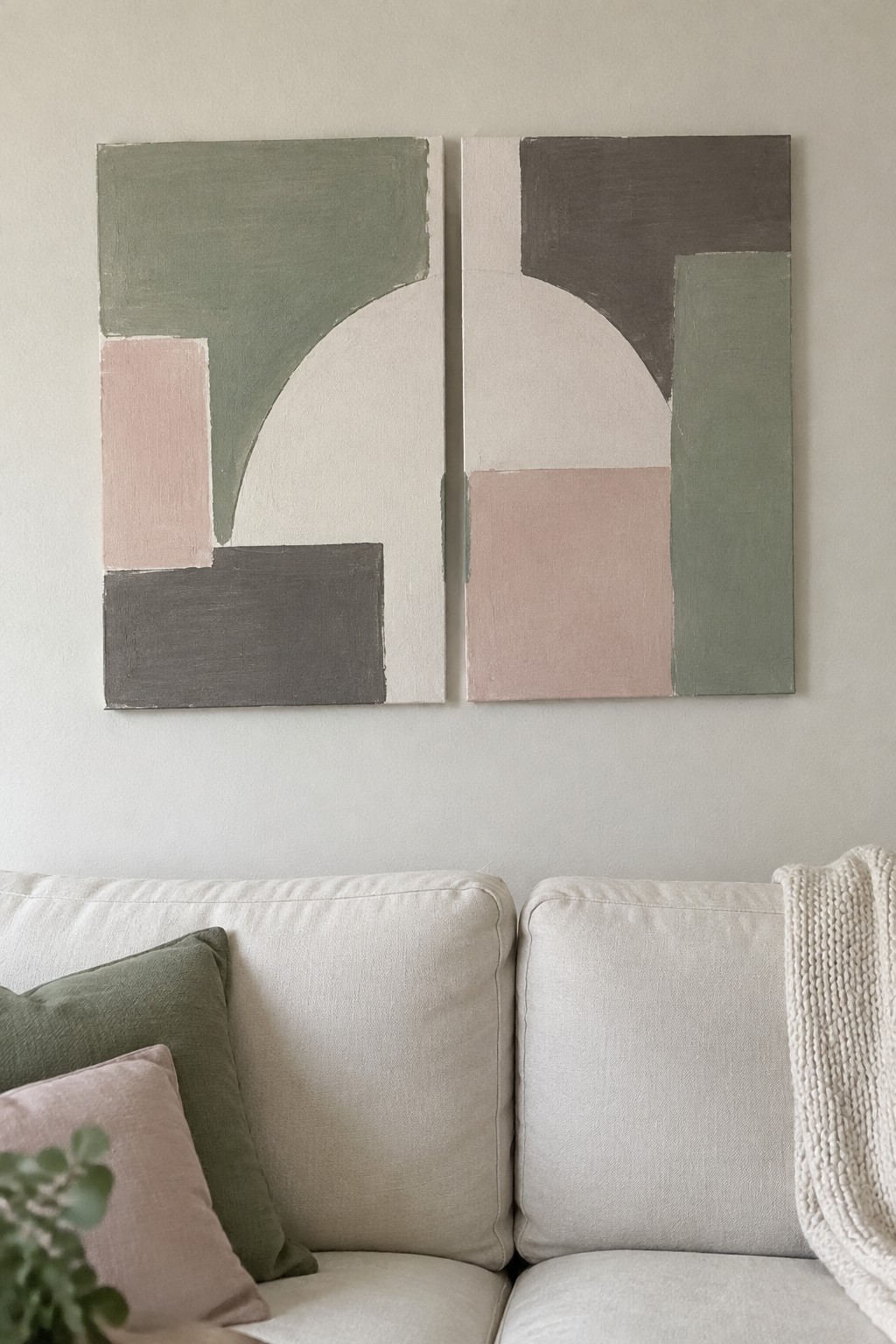 Two abstract paintings in muted greens and pinks above a beige sofa with pillows.