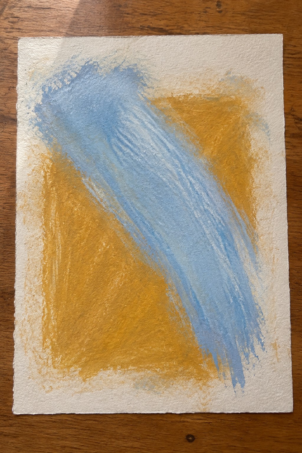 Abstract blue and yellow brushstrokes on textured white paper over wood