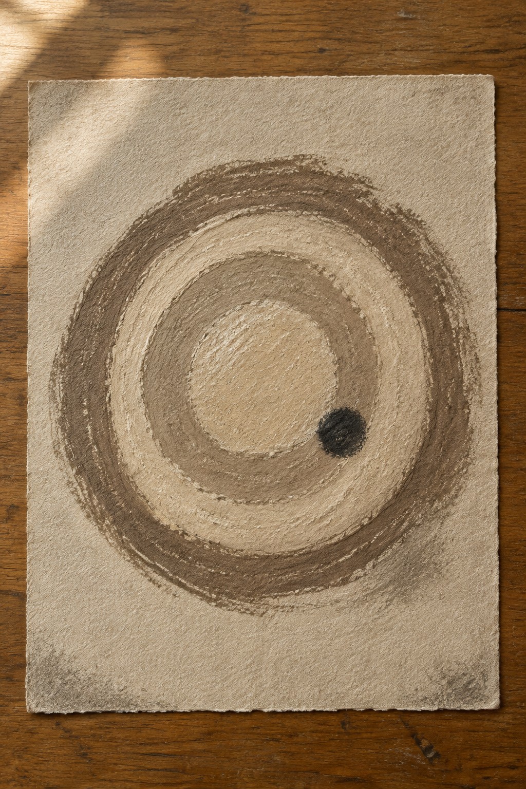 Concentric brown circles with off-center black dot on textured beige paper over wood