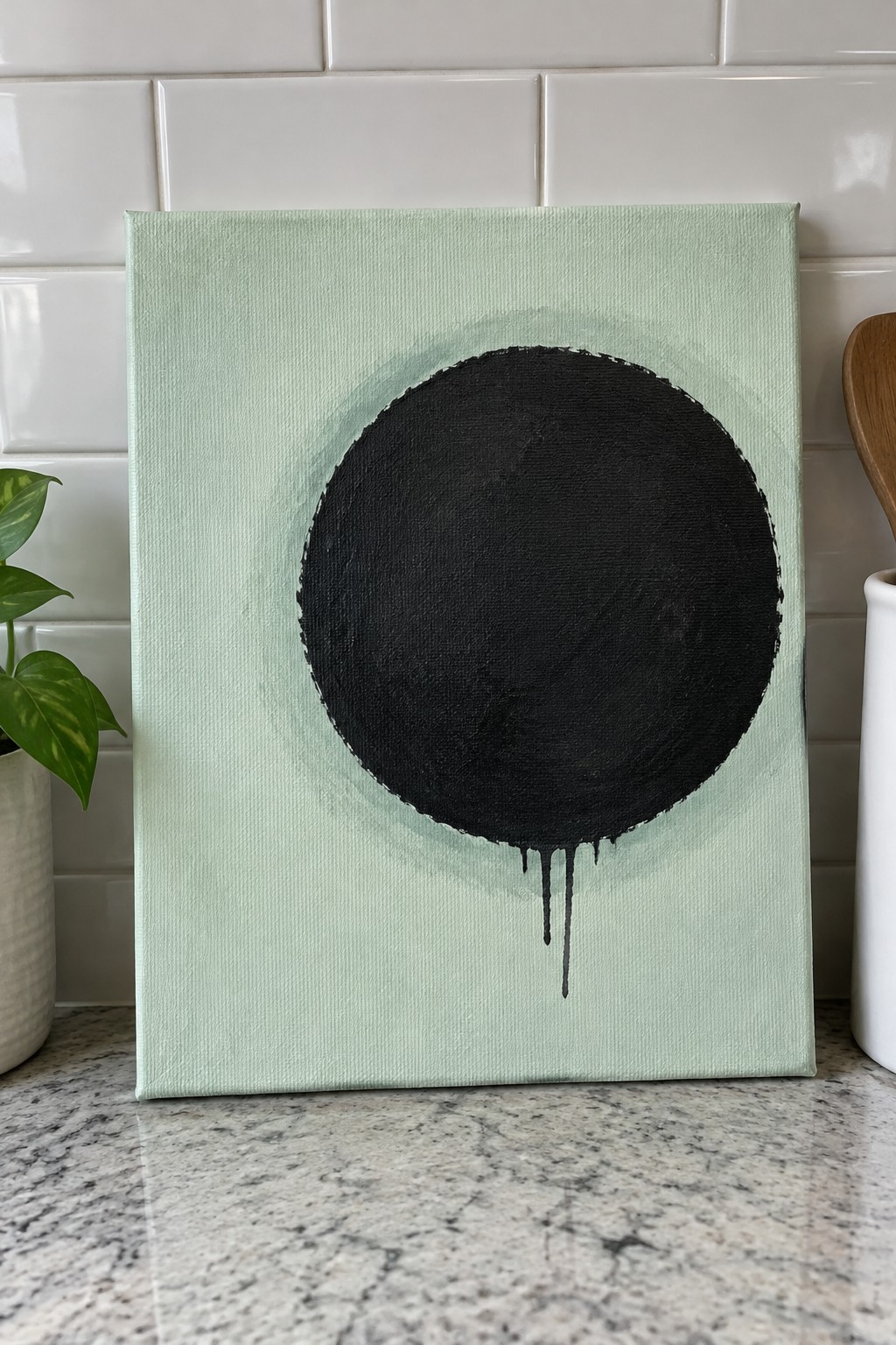 Mint green canvas with large black dripping circle and faint halo on kitchen counter
