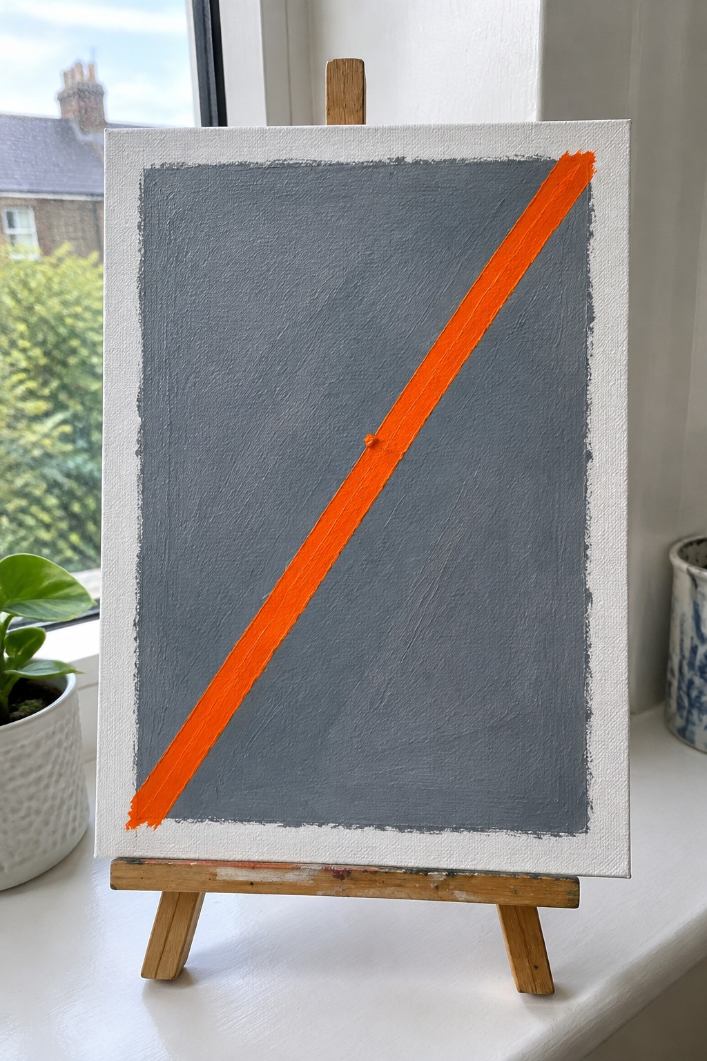 Orange diagonal stripe across gray canvas on wooden easel by window