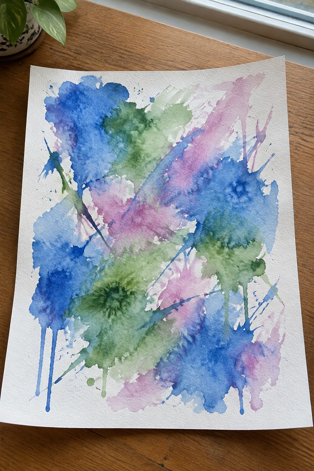 Abstract watercolor painting with blue, green, pink splashes and drips on paper