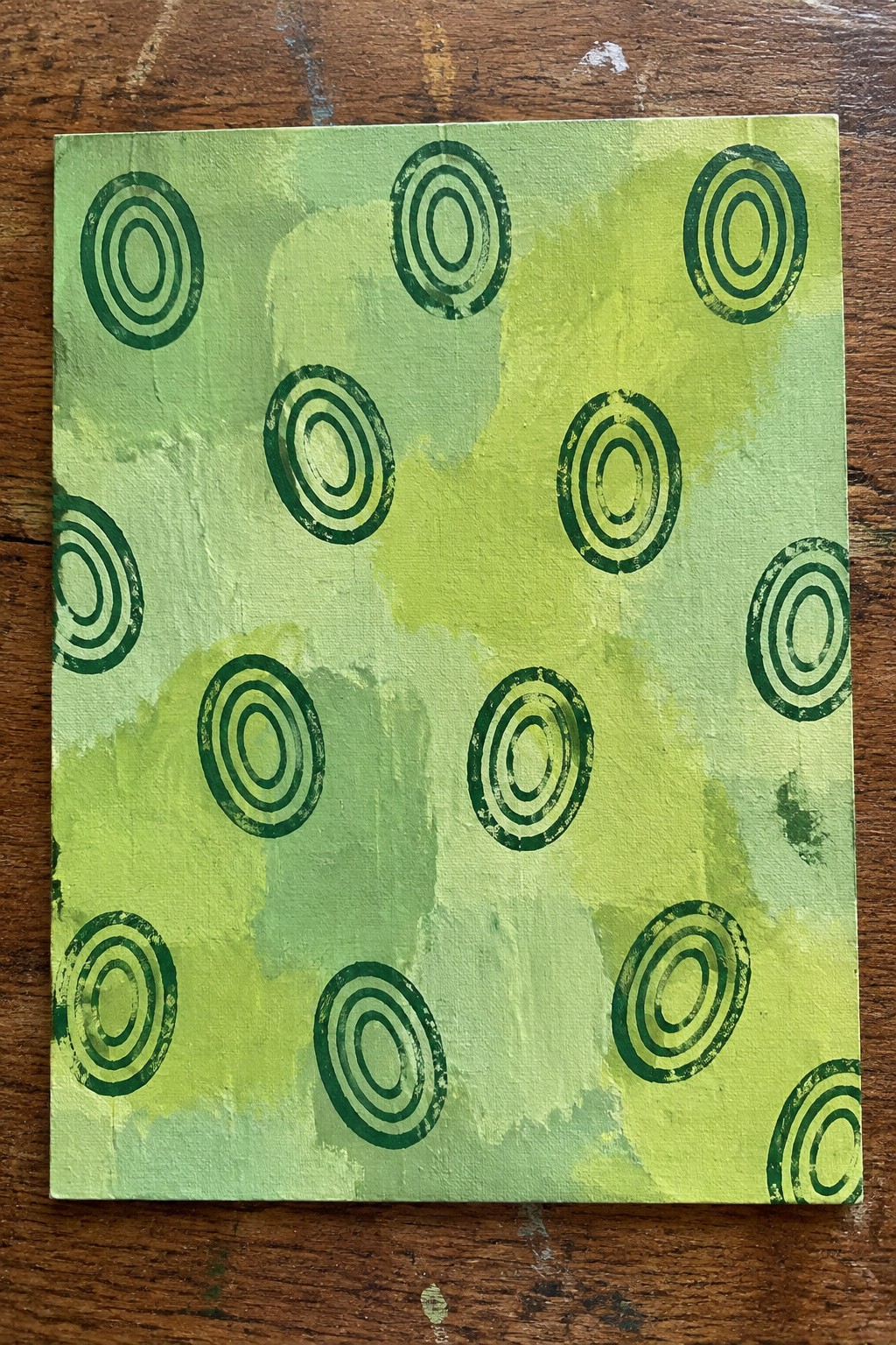 Green abstract painting with scattered dark green concentric circles on wood.