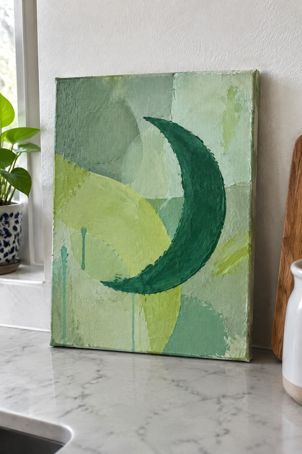 Abstract green canvas painting with crescent shape and drips on marble countertop
