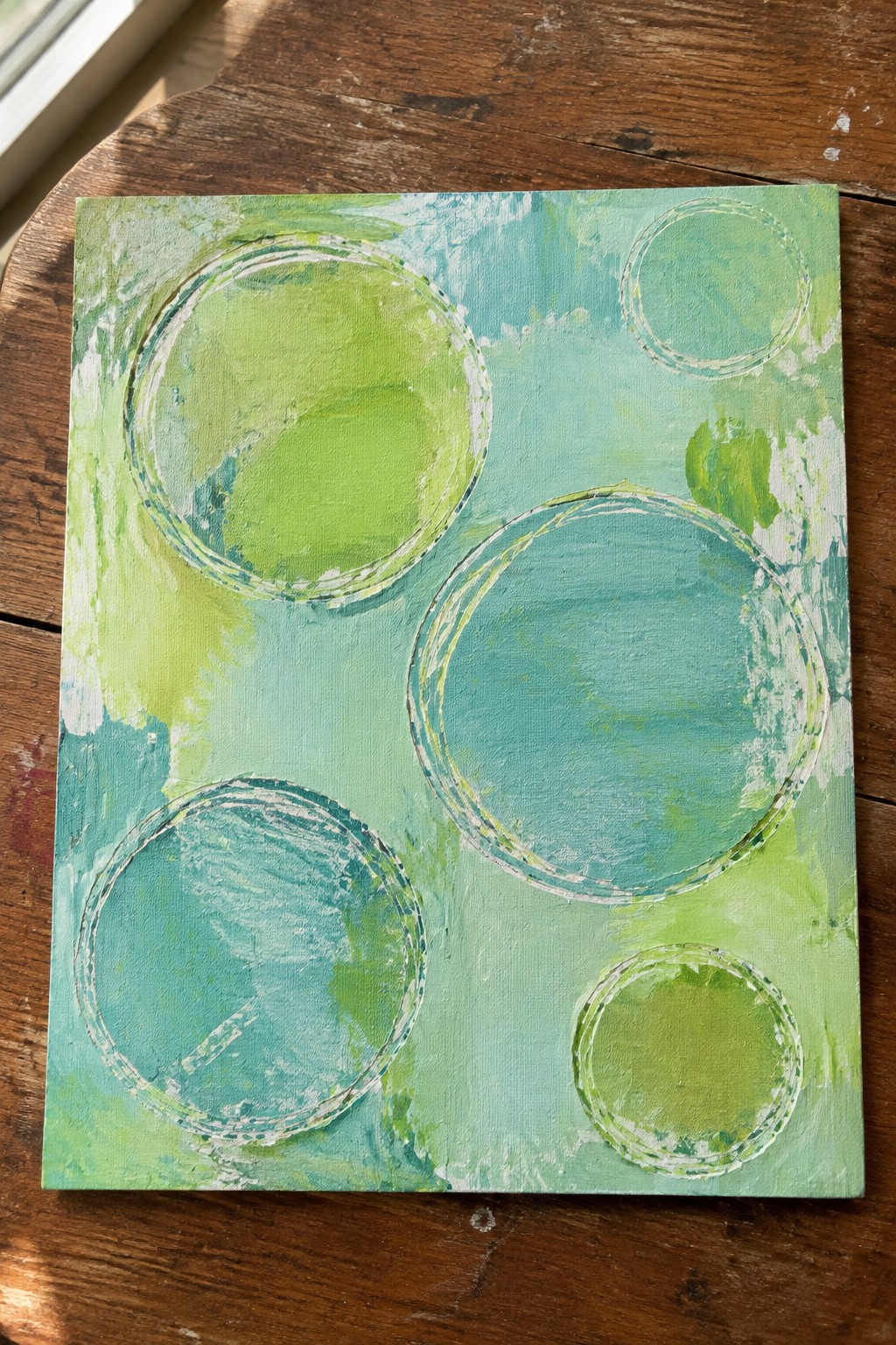 Abstract painting with overlapping green and turquoise circles on wooden surface