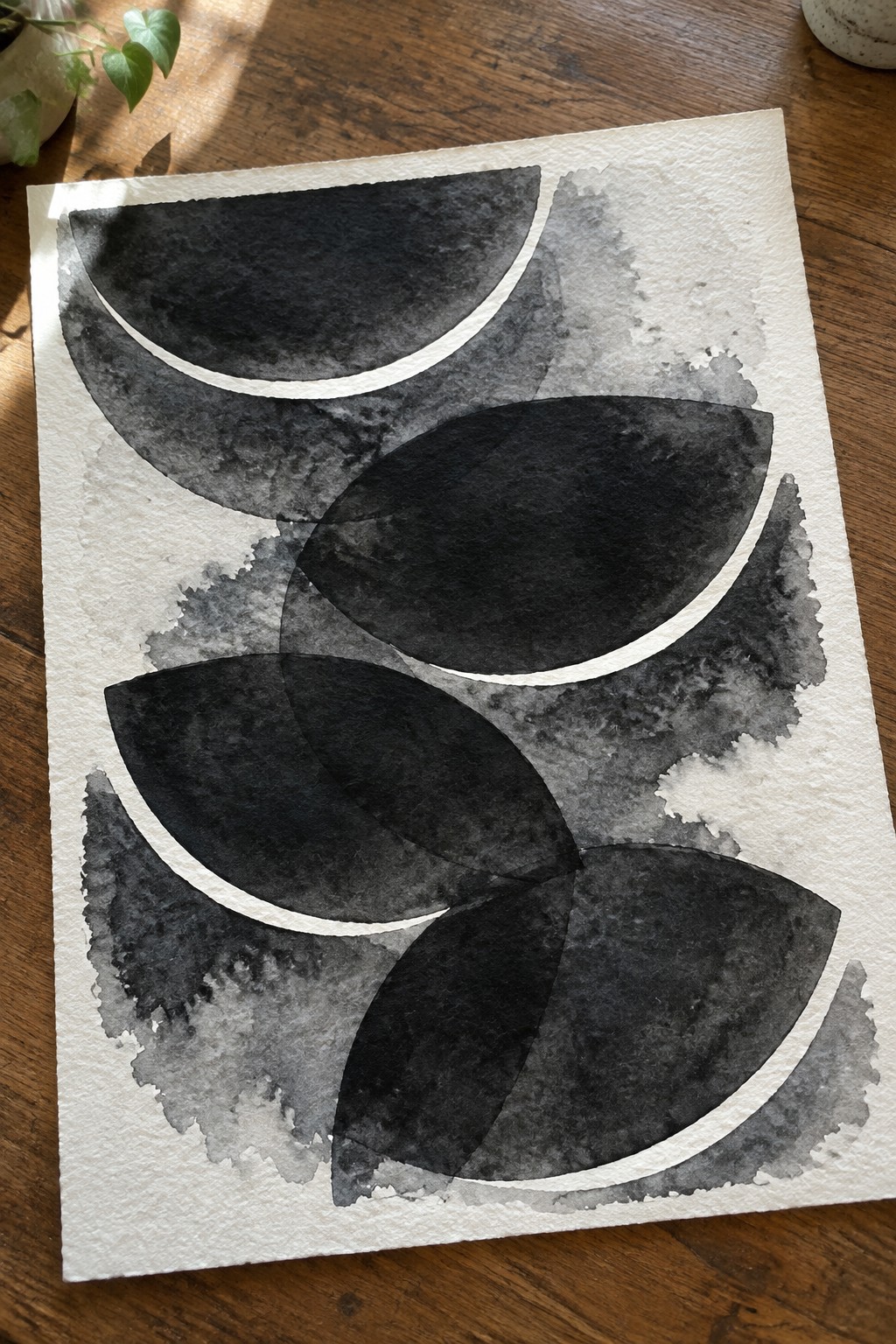 Abstract black watercolor shapes overlapping on white paper over wooden table