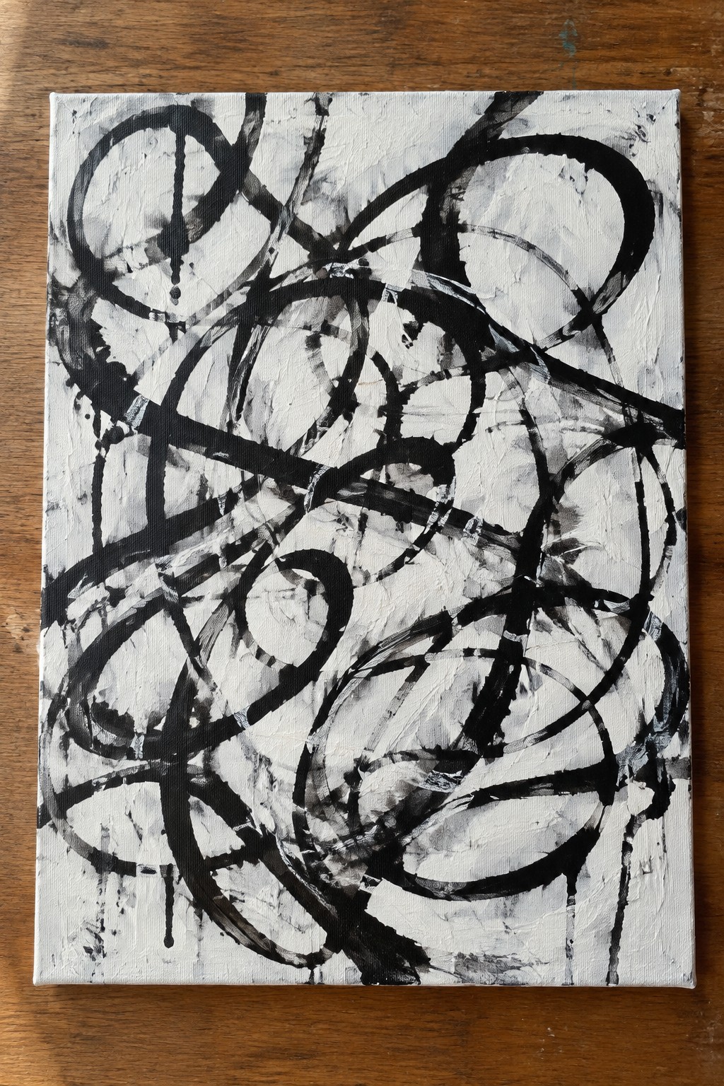 Abstract black brushstrokes and loops on textured white canvas atop wood