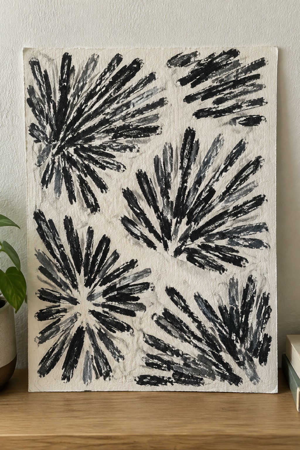 Abstract black brushstrokes on white canvas atop wooden surface with plant