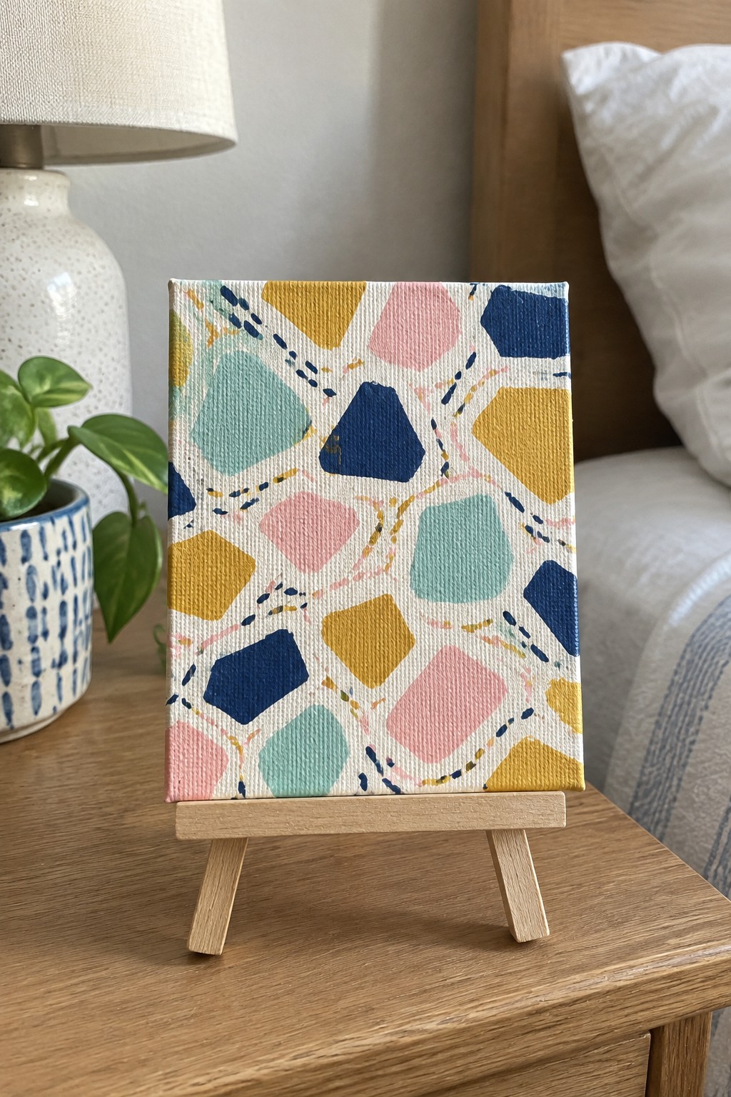 Colorful abstract painting with geometric shapes in blue, pink, and yellow on wooden easel