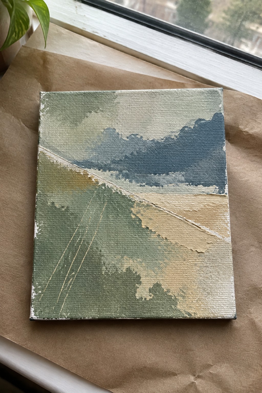 Abstract landscape canvas painting in blues and greens on brown paper by window