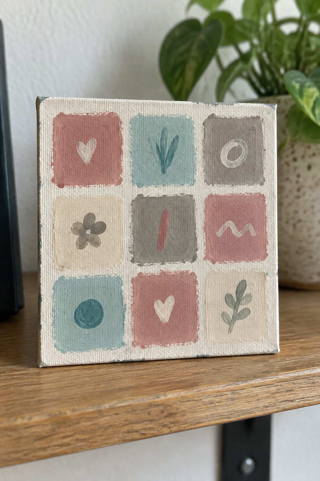 Small canvas with nine painted squares of hearts, flowers, leaves and shapes in muted tones
