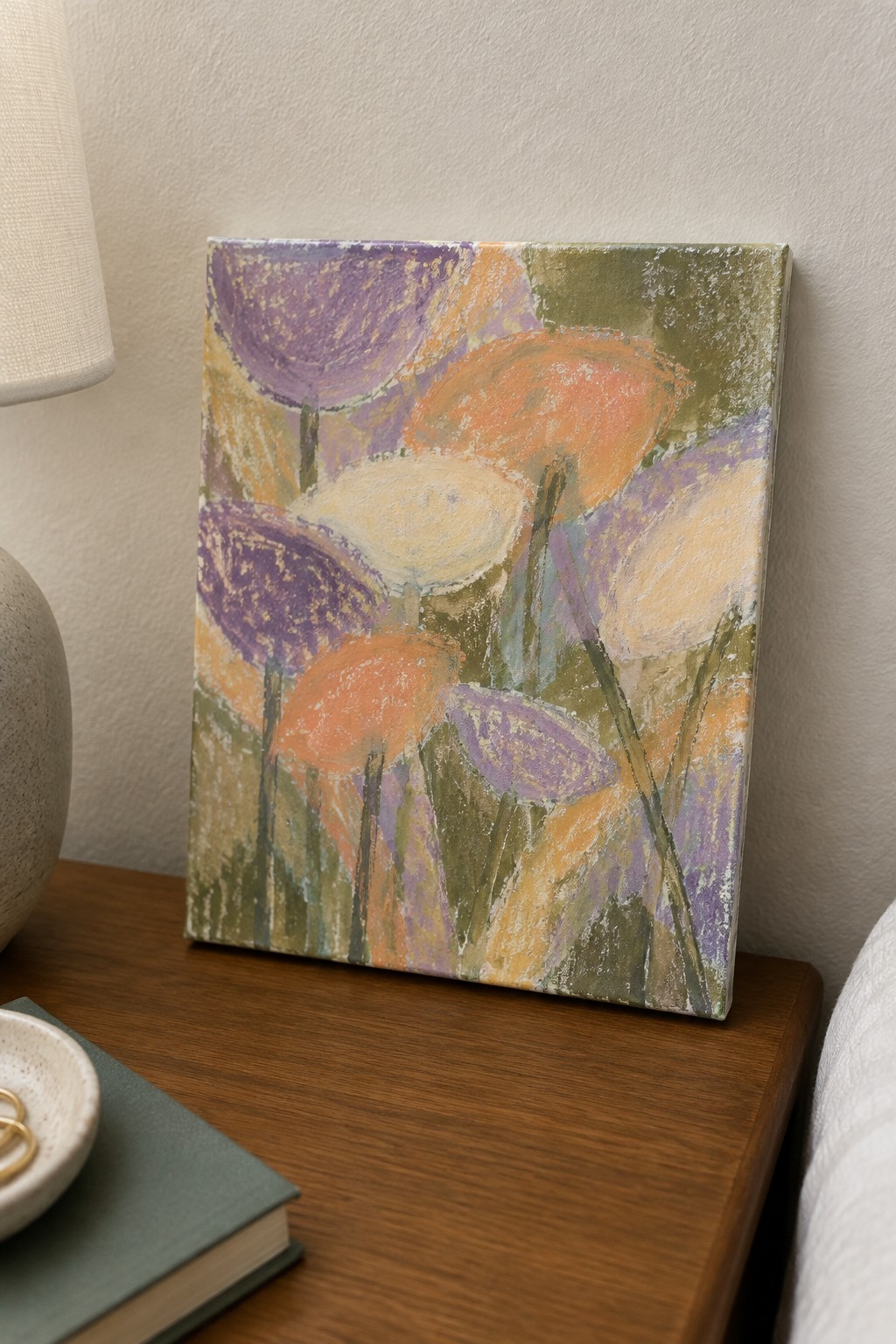 Abstract painting with purple orange and white flowers on wooden nightstand beside lamp