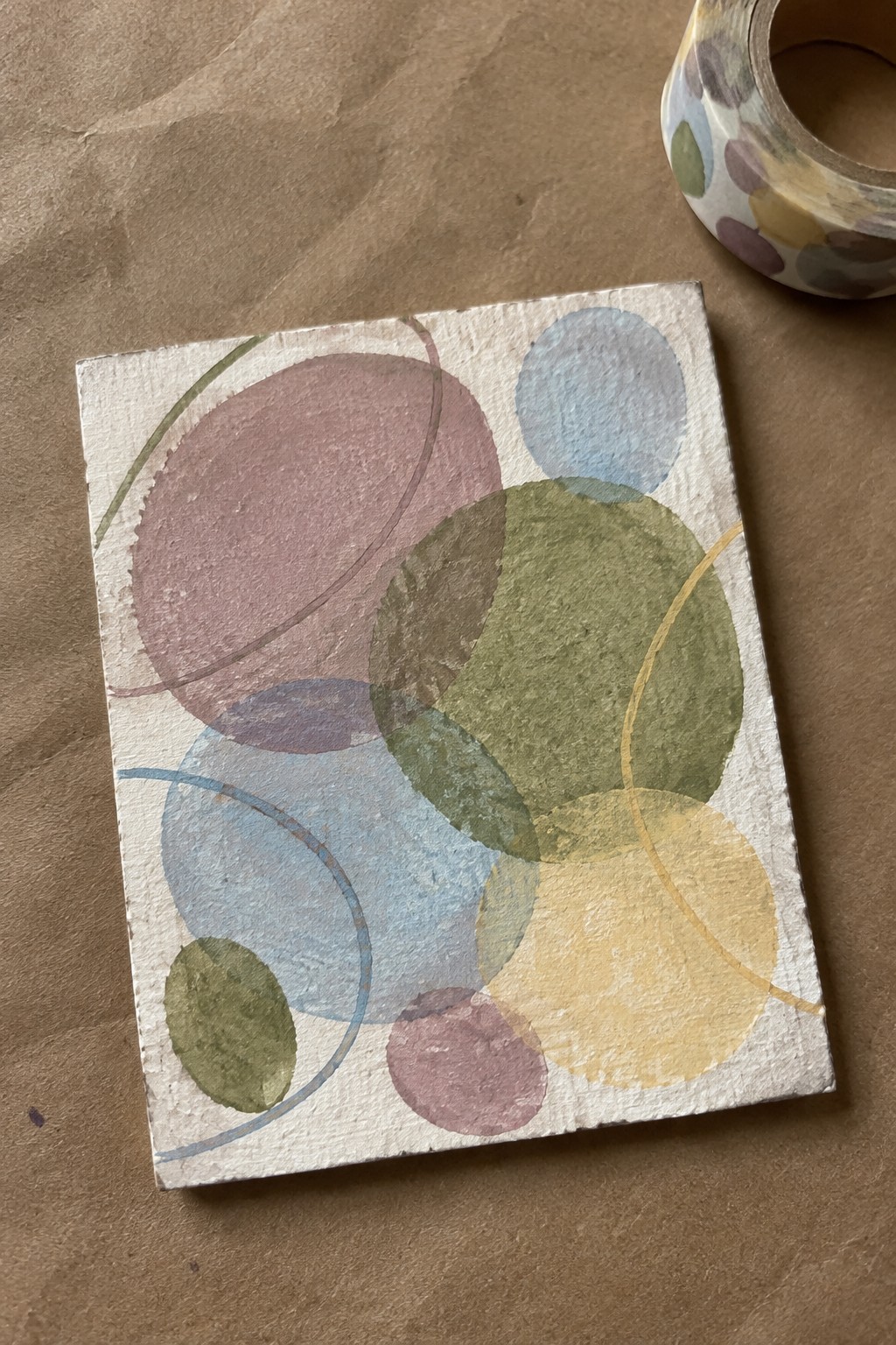 Abstract painting of overlapping colorful circles beside polka dot washi tape on brown paper