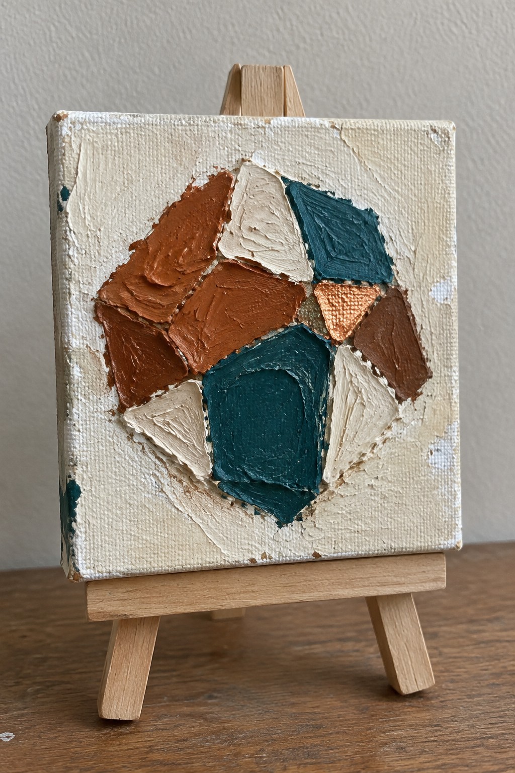 Abstract impasto painting with orange, teal, beige, and copper shapes on wooden easel.